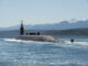 Submarino nuclear USS Nebraska da classe Ohio navegando na superfície com tripulação visível, montanhas ao fundo
