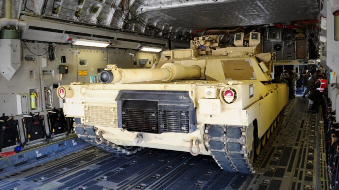 Tanque militar M1 Abrams sendo transportado dentro de um avião de carga com militares ao fundo.