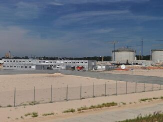 Imagem panorâmica do terminal de GNL em Świnoujście, mostrando tanques de armazenamento, construções auxiliares e guindastes de construção, com céu azul ao fundo.