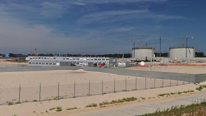 Terminal de GNL em Świnoujście, Polônia Imagem panorâmica do terminal de GNL em Świnoujście, mostrando tanques de armazenamento, construções auxiliares e guindastes de construção, com céu azul ao fundo.