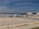 Imagem panorâmica do terminal de GNL em Świnoujście, mostrando tanques de armazenamento, construções auxiliares e guindastes de construção, com céu azul ao fundo.