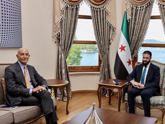 Ahmed al-Sharaa em reunião com Tom Barrack, maio de 2025, com a bandeira da Síria ao fundo.