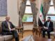 Ahmed al-Sharaa em reunião com Tom Barrack, maio de 2025, com a bandeira da Síria ao fundo.