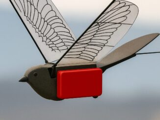 Drone biomimético voando, com asas transparentes que imitam asas de pássaro e corpo preto com um componente vermelho destacado.