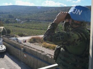 Soldado da ONU da UNIFIL observa a fronteira sul do Líbano usando binóculos, com veículo blindado da ONU ao fundo.