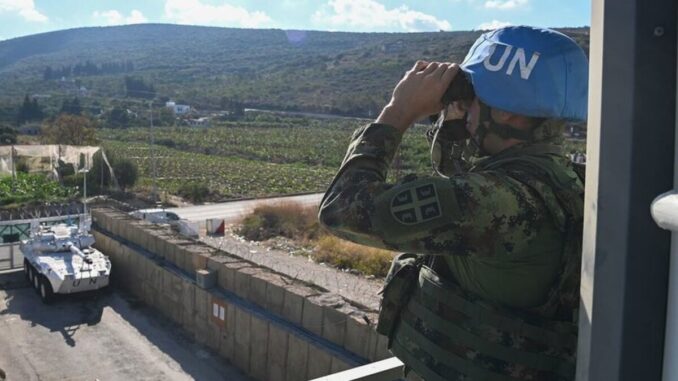 Soldado da ONU da UNIFIL observa a fronteira sul do Líbano usando binóculos, com veículo blindado da ONU ao fundo.