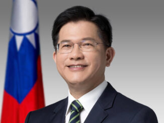 Retrato oficial de Lin Chia-lung, Ministro das Relações Exteriores de Taiwan, vestindo terno escuro e gravata, com a bandeira de Taiwan ao fundo.