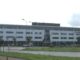 Prédio moderno da sede da ASML em Veldhoven, Holanda, com fachada branca e janelas de vidro, mostrando bandeiras na frente e carros estacionados ao redor.