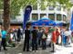 Stand informativo do partido AfD em Hannover com manifestação de oposição ao fundo, ilustrando crescimento da extrema-direita na Alemanha.
