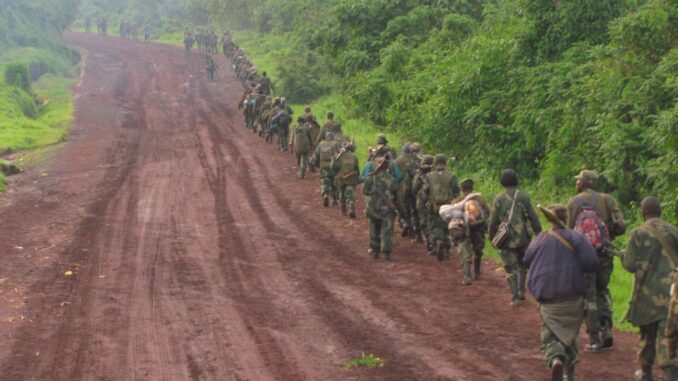 M23 em Movimento: Conflito no Leste da RDC Combatentes do grupo rebelde M23 marchando em fila por uma estrada de terra no leste da República Democrática do Congo, cercados por vegetação densa.