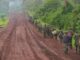 Combatentes do grupo rebelde M23 marchando em fila por uma estrada de terra no leste da República Democrática do Congo, cercados por vegetação densa.