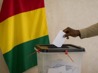 Pessoa depositando voto em urna com a bandeira da Guiné ao fundo, simbolizando o referendo constitucional de 2025.