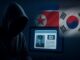 Hacker encapuzado diante de tela de computador exibindo identidade militar falsa, com bandeiras da Coreia do Norte e Coreia do Sul ao fundo, simbolizando ataque cibernético.