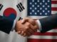 Aperto de mãos entre representantes da Coreia do Sul e dos Estados Unidos, com as bandeiras dos dois países ao fundo, simbolizando cooperação e diálogo diplomático.