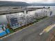 Navio transportando módulos de infraestrutura de GNL em um porto canadense, com montanhas ao fundo e contêineres no cais.