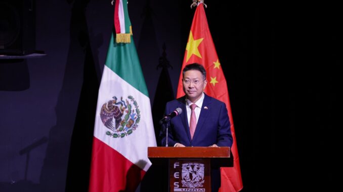 Relações Comerciais China-México 2025 Representante da China discursando em frente às bandeiras do México e da China em evento oficial.
