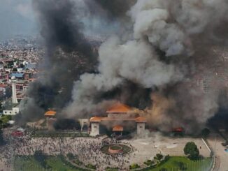 Edifício do Parlamento do Nepal em chamas durante protestos em Kathmandu; grande fumaça negra sobe ao céu enquanto manifestantes se reúnem na frente do prédio.