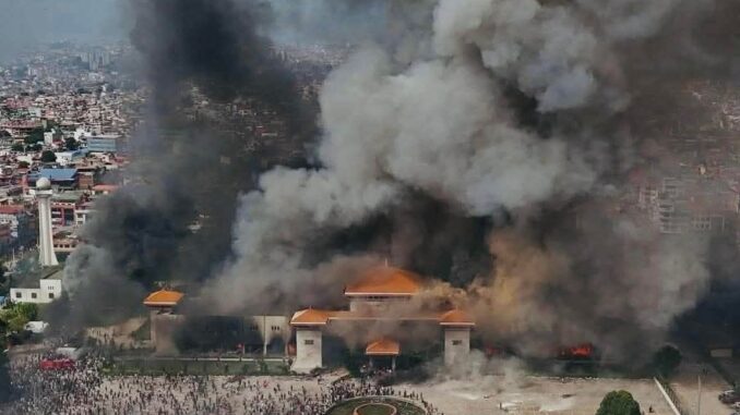 Crise no Nepal: Parlamento em Chamas e Renúncia do Primeiro-Ministro Edifício do Parlamento do Nepal em chamas durante protestos em Kathmandu; grande fumaça negra sobe ao céu enquanto manifestantes se reúnem na frente do prédio.