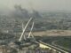 Fumaça preta sobe sobre a cidade de Doha, Catar, após explosões de ataque aéreo, com destaque para o icônico arco da cidade ao fundo.