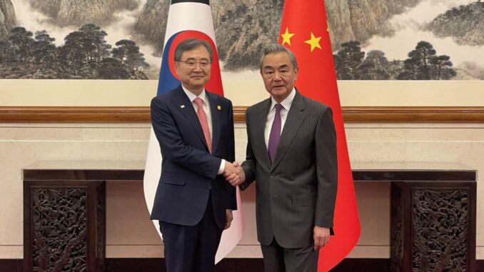 O ministro das Relações Exteriores da Coreia do Sul, Cho Hyun, cumprimenta o ministro chinês Wang Yi em Pequim, com as bandeiras da Coreia do Sul e da China ao fundo.