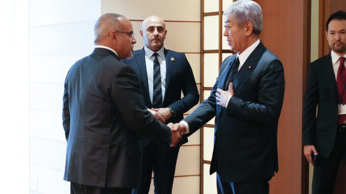 Ministro japonês Takeshi Iwaya cumprimenta representante diplomático durante encontro oficial, enquanto assessores observam ao fundo.