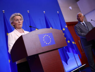 Ursula von der Leyen em coletiva de imprensa ao lado de autoridades europeias, com bandeiras da União Europeia ao fundo.