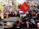Membros e apoiadores do Hezbollah em um desfile no Líbano acenando com bandeiras vermelhas e amarelas.