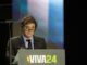 Javier Milei discursando em púlpito com microfone, usando óculos e terno, durante evento VIVA24.
