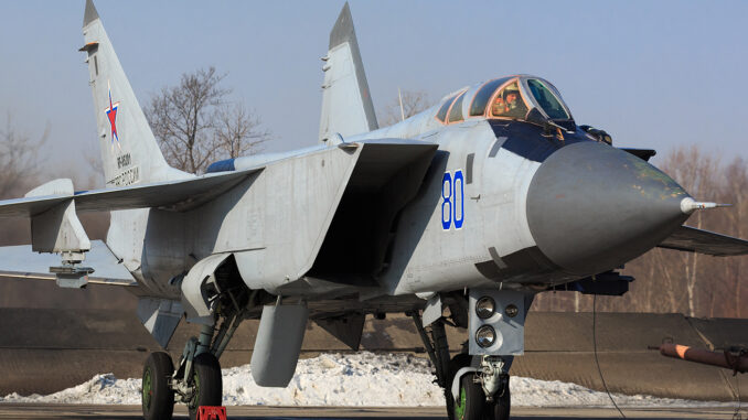 MiG-31 da Força Aérea Russa Caça russo Mikoyan-Gurevich MiG-31 estacionado no solo com trem de pouso visível, asas abertas e cabine ocupada pelo piloto.