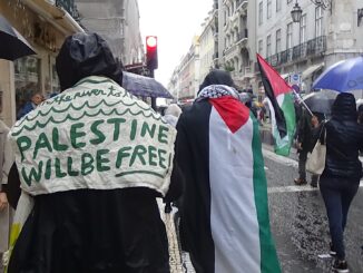 Manifestantes em Lisboa participando de protesto em apoio à Palestina, com bandeiras palestinas e cartazes com a mensagem "Palestine Will Be Free".