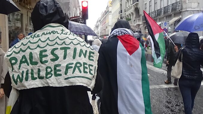 Protesto em Lisboa em apoio à Palestina Manifestantes em Lisboa participando de protesto em apoio à Palestina, com bandeiras palestinas e cartazes com a mensagem "Palestine Will Be Free".
