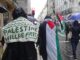 Manifestantes em Lisboa participando de protesto em apoio à Palestina, com bandeiras palestinas e cartazes com a mensagem "Palestine Will Be Free".